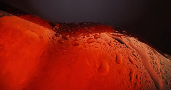 Slow motion cold brown glass beer bottle with condensation against blurred blue studio background, probe view.