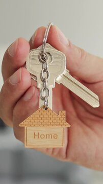 Hand holds keys for home buying. Person displays a keyring and wooden house token indoors for mortgage, property sales, rental listings, and moving. A practical real estate concept.