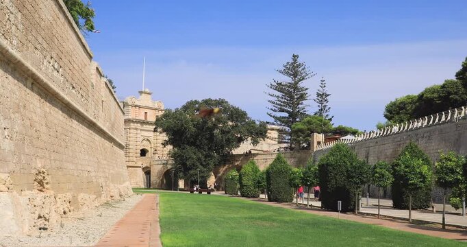 Townscape of Mdina in Malta Island: view of the moat with surrounding fortified walls and the medieval entrance in the background.