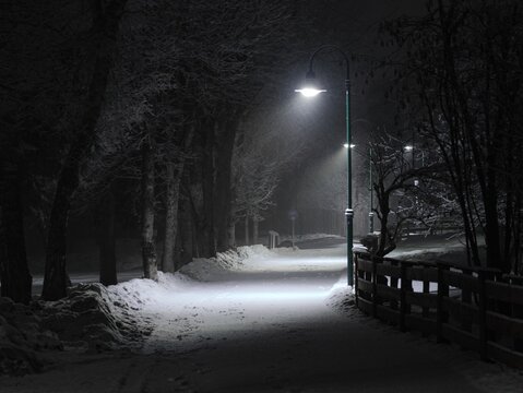 A snow-covered road at night illuminated by a bright street lamp.
