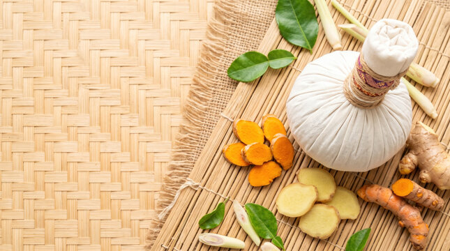 Herbal compress ball with turmeric root and ginger on woven bamboo mat.