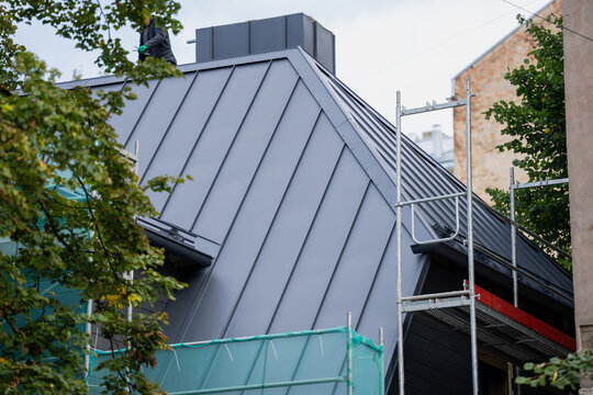 Worker at the ridge of a standing seam metal roof above scaffold access platforms, sheet metal roof covering and elevated access during building refurbishment