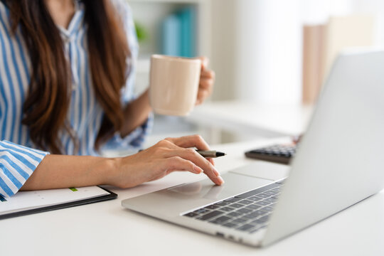  close up hands of woman working on her laptop at a table. working  remotely from home hand holding a coffee cup. people and lifestyle concepts
