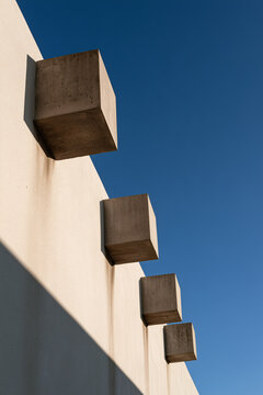 Projecting concrete drainage spouts along a rendered parapet against a deep blue sky

