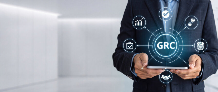 Businessman using digital tablet for GRC Governance Risk and Compliance concept, showing icons for audit, risk management, and regulatory compliance on a futuristic interface in a corporate office.