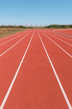 Empty red running track with white lane markings under clear blue sky at outdoor sports facility
