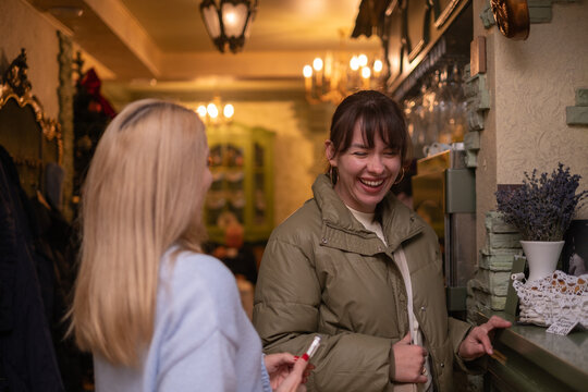 Two women talk and laugh in a cozy cafe with warm lighting and a rustic interior in the evening