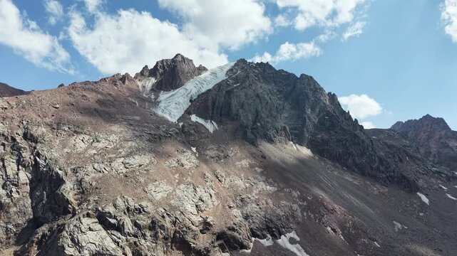 Cinematic drone flyover over rocky peaks, Oktyabrskaya cave, and shrinking ice blocks near Talgar Pass at 3400 meters altitude, revealing climate change and glacier melting in Tian Shan mountains near