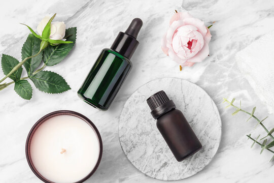 Essential oil bottles with aroma candle, and pink roses on white marble table