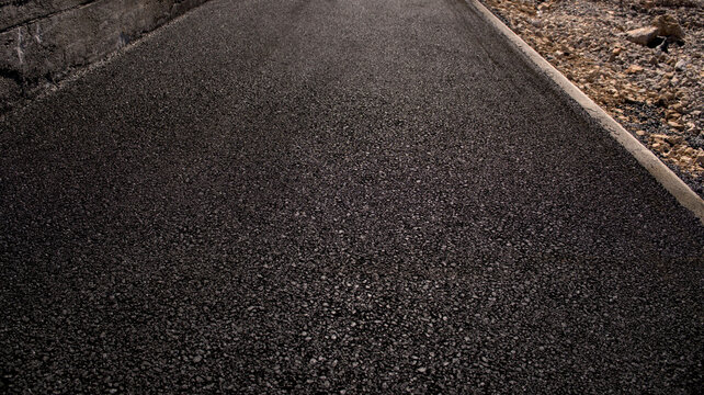 Smooth freshly laid black asphalt road texture with concrete curb. Perfect for road construction, paving, urban infrastructure, and civil engineering visuals.