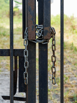 Strong iron chain links wrapped around a rusty wrought iron gate post to restrict entry and access.