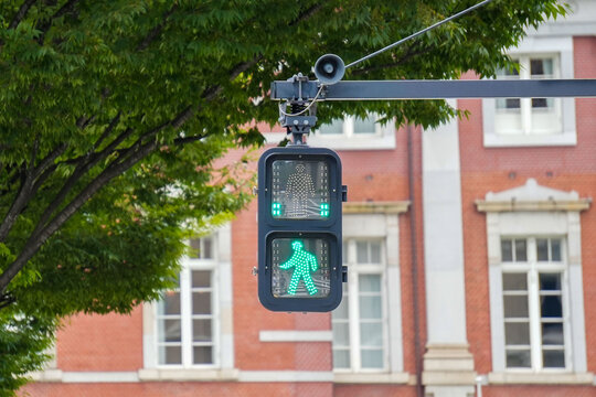 Green pedestrian crossing signal illuminated in front of the historic red brick Tokyo Station building, Japan