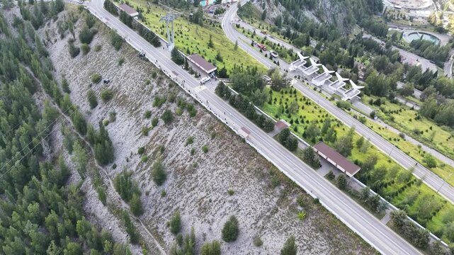 Cinematic top-down drone flyover directly above crest of massive embankment mudflow control dam with steep slopes, protective forest, and access road in Almaty, Kazakhstan at summer sunset