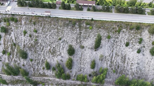 Cinematic top-down drone flyover directly above crest of massive embankment mudflow control dam with steep slopes, protective forest, and access road in Almaty, Kazakhstan at summer sunset