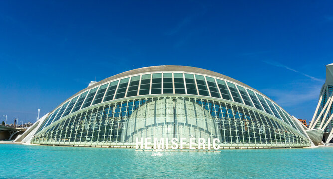 L'Hemisf&egrave;ric, a modern architectural landmark designed by Santiago Calatrava, standing elegantly in the shallow reflecting pool under a clear blue sky in the City of Arts and Sciences