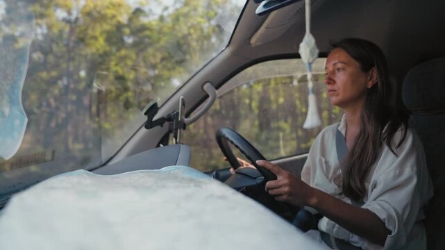 Woman drives a van during the day with a map on the dashboard while traveling along a road through a scenic green forest area