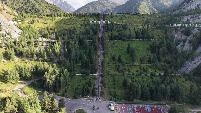 Cinematic drone flyover moving toward massive concrete stairways leading up to Medeu mudflow protection dam with outdoor sports facility at the base in Almaty, Kazakhstan at summer sunset.