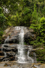 Tropical jungle waterfall in Thailand surrounded by lush green rainforest, moss-covered rocks, dense vegetation, and flowing water. The natural cascade creates a peaceful and refreshing scene © Yuliia