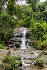 Tropical jungle waterfall in Thailand surrounded by lush green rainforest, moss-covered rocks, dense vegetation, and flowing water. The natural cascade creates a peaceful and refreshing scene © Yuliia