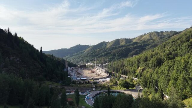ALMATY, KAZAKHSTAN - AUGUST 2026: Aerial drone flyover above circular water reservoir near Medeu mudflow control dam and high-altitude ice rink during renovation process in Medeu gorge at summer eveni
