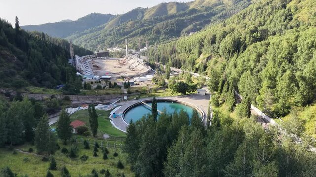 ALMATY, KAZAKHSTAN - AUGUST 2026: Aerial drone flyover above circular water reservoir near Medeu mudflow control dam and high-altitude ice rink during renovation process in Medeu gorge at summer eveni