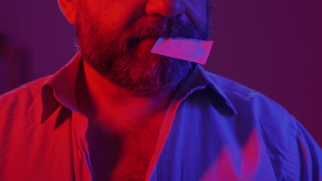 Protection, safe love and contraceptive concept. Bearded man holding latex condom package in mouth undressing his shirt