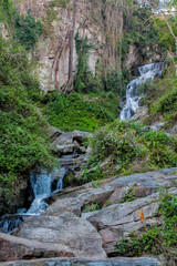 Tropical jungle waterfall in Thailand surrounded by lush green rainforest, moss-covered rocks, dense vegetation, and flowing water. The natural cascade creates a peaceful and refreshing scene © Yuliia