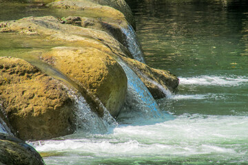 Tropical jungle waterfall in Thailand surrounded by lush green rainforest, moss-covered rocks, dense vegetation, and flowing water. The natural cascade creates a peaceful and refreshing scene © Yuliia