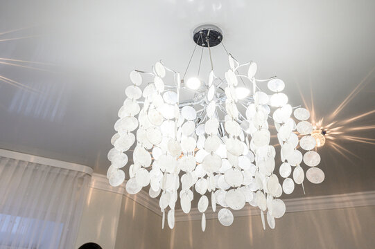 Elegant chandelier with cascading capiz shells, clear rods, and glowing bulbs; suspended from sleek ceiling mount; soft light refracts through translucent discs