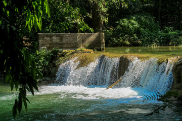 Tropical jungle waterfall in Thailand surrounded by lush green rainforest, moss-covered rocks, dense vegetation, and flowing water. The natural cascade creates a peaceful and refreshing scene © Yuliia