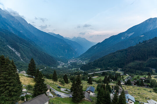 Tyrol, Austria: Expansive mountain panorama reveals a deep green valley, alpine village, winding roads, scattered houses and layered peaks fading into evening haze. Strong travel image for scenic road