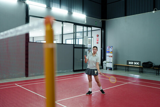 Young Asian woman practicing badminton forehand swing on indoor court during training session