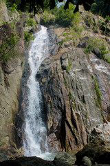 Tropical jungle waterfall in Thailand surrounded by lush green rainforest, moss-covered rocks, dense vegetation, and flowing water. The natural cascade creates a peaceful and refreshing scene © Yuliia