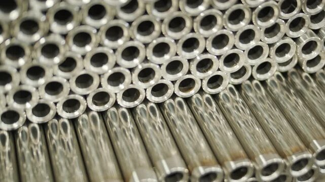 Close-up of a large stack of shiny, polished stainless steel metal tubes arranged in a uniform pattern. Industrial background showing clean cylindrical pipes ready for manufacturing or construction.