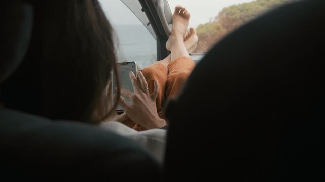 Relaxed person resting feet on car dashboard while checking a digital map on a mobile phone during a daylight travel adventure