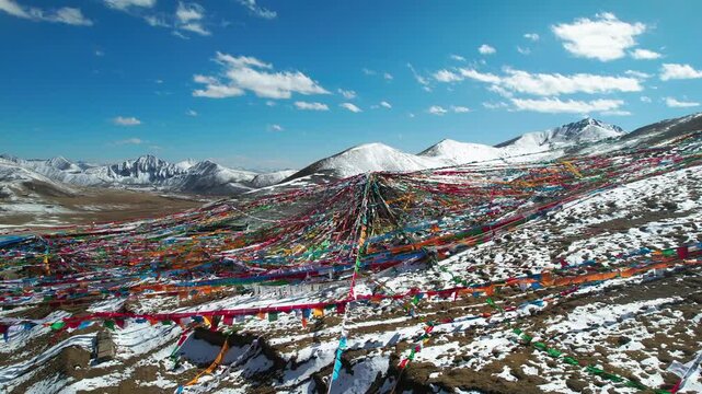 Aerial crossing colorful prayer flags toward a snowy plateau