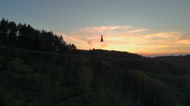 Highline Aerial Shot. Brave Girl Tightrope Walker is on a rope stretched between Mountains at high altitude, Sunset Time