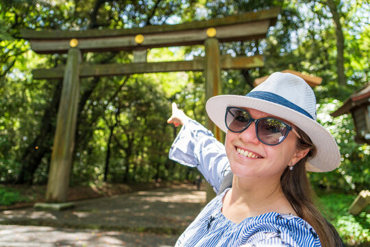 Mujer turista con sombrero tom&aacute;ndose una selfie frente a una gran puerta torii, entrando al santuario de Meiji, en Tokio, Jap&oacute;n