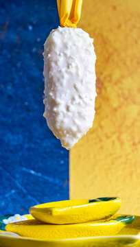 Lemon ice cream covered in white chocolate suspended on blue and yellow color block background