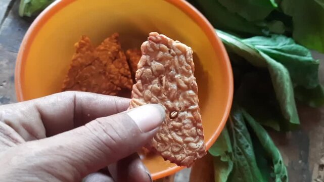 Hand Picking Fried Tempeh from Orange Bowl - Indonesian Traditional Food`
