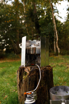 Vertical portrait of portable gas stove on wooden stump with metal windshield outdoor camping equipment forest background tourist cooking setup picnic wilderness nature exploration travel adventure li