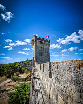 Polygonal keep tower and stone rampart walkway of medieval Ch&acirc;teau de Beaucaire with French flag under a blue sky in Gard, France.