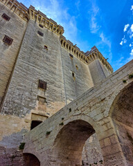 Fototapeta premium Low-angle view of the medieval Château de Tarascon fortress walls and stone arch bridge under a blue sky in Provence, France.