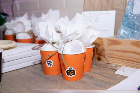 orange cups with themed stickers, bundles of sweets tied with string, Halloween treats, festively wrapped surprise bundles for children