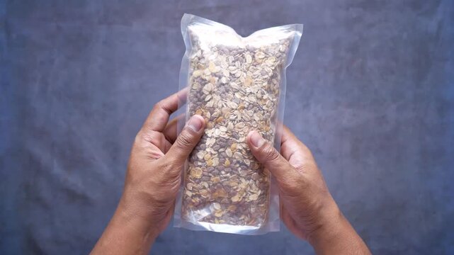 Hands holding vacuum sealed bag of mixed oats and nuts on dark background