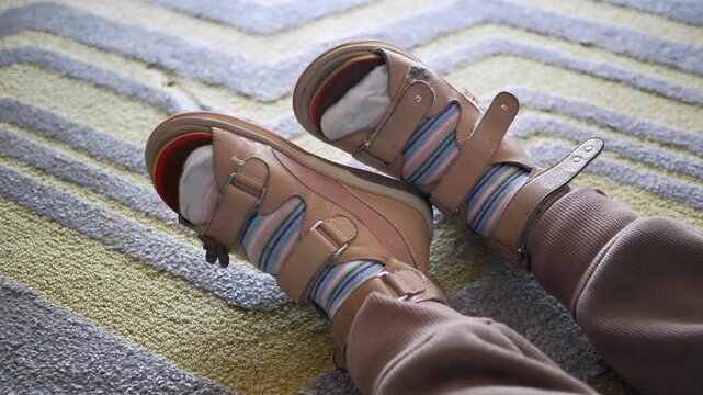 Pair of feet wearing orthopedic sandals and striped socks moving on a rug
