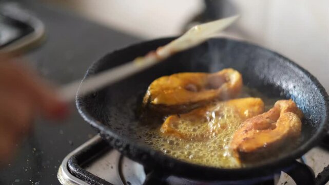 Chef frying fish pieces in hot oil in iron skillet on gas stove with cinematic motion and sizzling bubbles