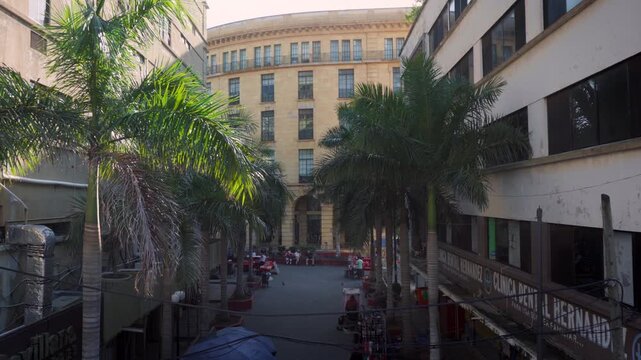 Shaded pedestrian alleyway in Tampico historic center looking toward sunlight SAT government building with people walking under bright sky