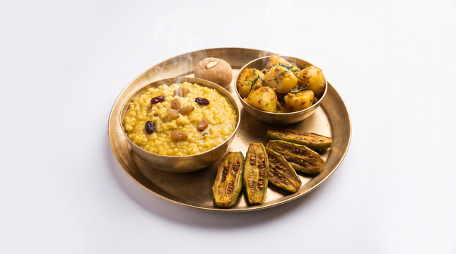 Close-up shot of steaming hot Durga Puja prasad thali with ghee-infused khichuri, aloo dum, crispy pointed gourd fry, pure white background