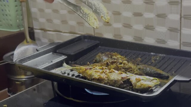 Hand flips fish on grill with tongs